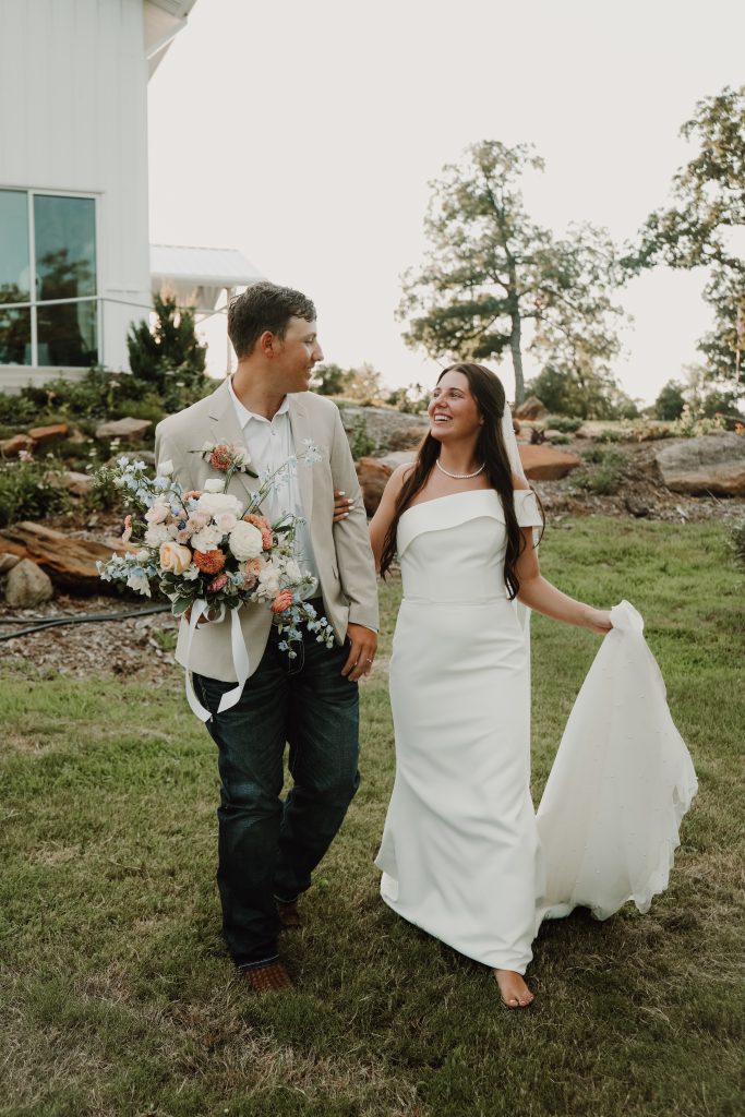 Bristow couple looking into each other's eyes after their joyous wedding ceremony. She is holding her train and he is holding her bouquet at Bella Rosa Venue near Tulsa OK